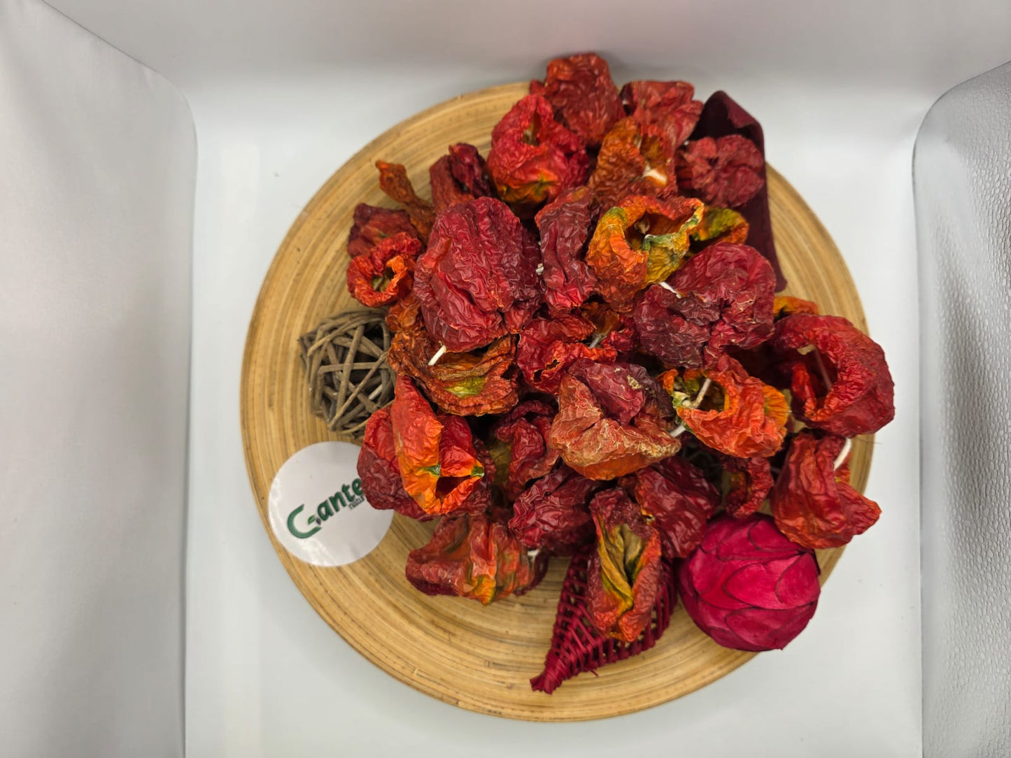 Getrocknete, scharfe Paprikaschoten in natürlicher, gerillter Struktur dekorativ auf einem Holzbrett mit Trockenblumen angerichtet, inklusive Gantep Naturel-Logo auf hellem Hintergrund.