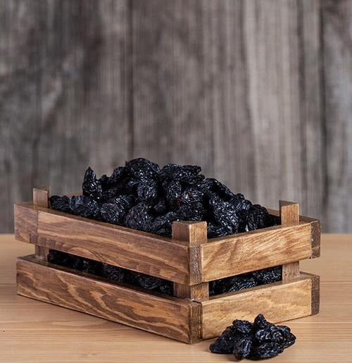 Getrocknete schwarze Trauben angerichtet in einer dekorativen Holzschale auf rustikalem Hintergrund.
