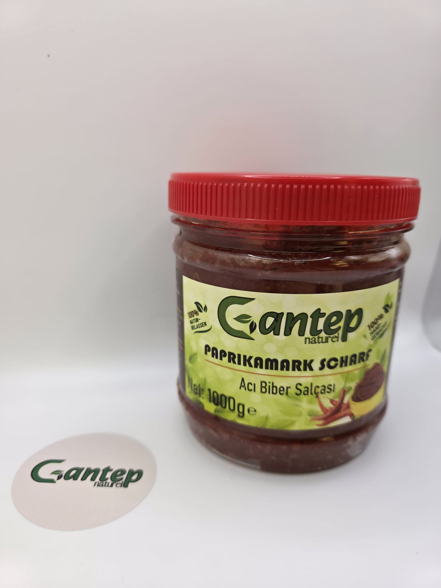 Gantep Naturel scharfer Paprikamark im 1000-g-PET-Behälter mit rotem Schraubdeckel; Frontansicht der Verpackung mit grünem Etikett und Produktdetails, fotografiert auf hellem Hintergrund.