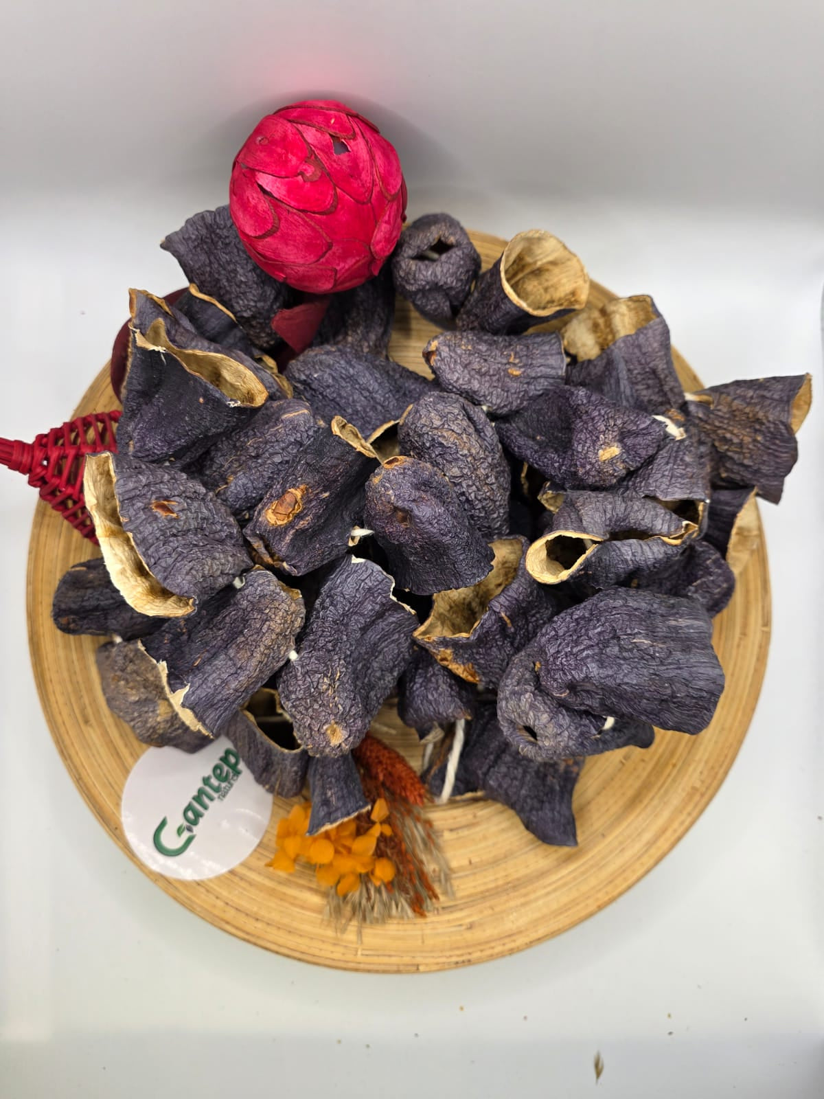 Getrocknete Auberginenhälften von Gantep Naturel, dekorativ auf einer Holzplatte mit floralen und farbigen Dekoelementen arrangiert, aus leicht erhöhter Perspektive fotografiert.