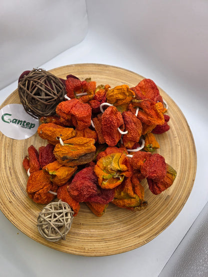 Dekorativ angerichtete milde getrocknete Paprika auf einer runden Holzplatte mit dekorativen Trockenästen, Draufsicht mit Logo von Gantep Naturel.