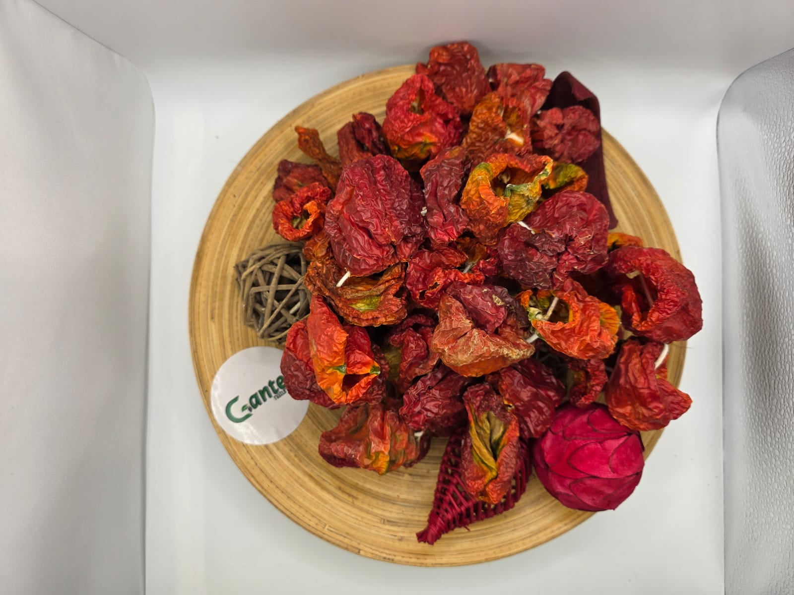 Getrocknete, scharfe Paprikaschoten in natürlicher, gerillter Struktur dekorativ auf einem Holzbrett mit Trockenblumen angerichtet, inklusive Gantep Naturel-Logo auf hellem Hintergrund.