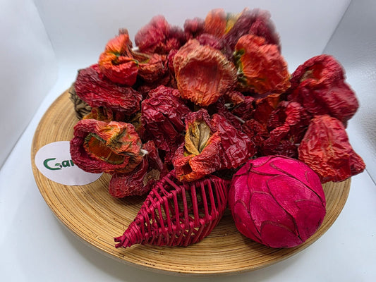 Seitlich fotografierte Nahaufnahme dekorativ arrangierter getrockneter Paprika auf einem Holzbrett, kombiniert mit Trockenblumen und rosafarbenen Dekoelementen.
