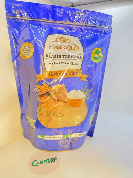 Vorderseite der Haşiroğlu Klasik Tarhana – Yoghurt Chips Classic Verpackung; blauer Standbeutel mit Abbildung von Joghurt und Tarhana-Flocken, goldfarbene Bannerbeschriftung und Angaben zu Protein- und Ballaststoffgehalt.