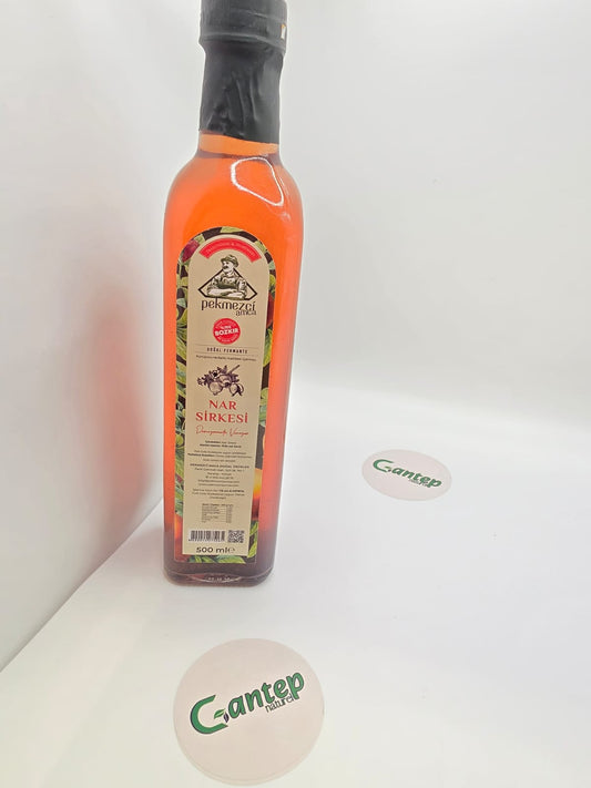 500-ml-Glasflasche Granatapfelessig Nar Sirkesi von Pekmezci Amca, transparent rotfarbener Essig, mit detailliertem Etikett und schwarzem Flaschenverschluss, fotografiert auf hellem Hintergrund.